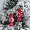 A set of two shiny red and white striped candy cane Christmas tree ornaments hanging on a green fir branch covered in artific