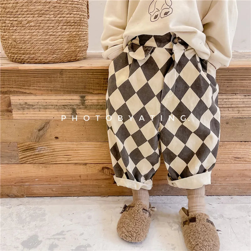 A child wearing brown and beige checkered harem pants with pockets, standing in front of a wooden step.
