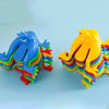 A set of colorful jumping frog toys in blue, yellow, and green are displayed against a light blue background.