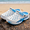 White and blue EVA slip-on sandals resting on a dark rock near the ocean.