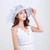A woman wearing a white dress and a sheer silver wide brim sun hat with ruffled mesh details.