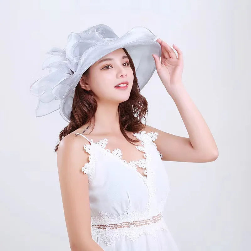 A woman wearing a white dress and a sheer silver wide brim sun hat with ruffled mesh details.