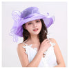 A woman models a purple organza sun hat with ruffled mesh and a white lace top.