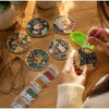 Hands are painting a festive diamond painting wooden ornament kit on a wooden surface.