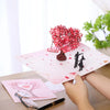 A pink pop-up love tree card featuring a red floral design and a silhouette of a couple.