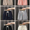 A collection of kids beach shorts in various colors including beige pink navy gray black and cream shown on hangers.