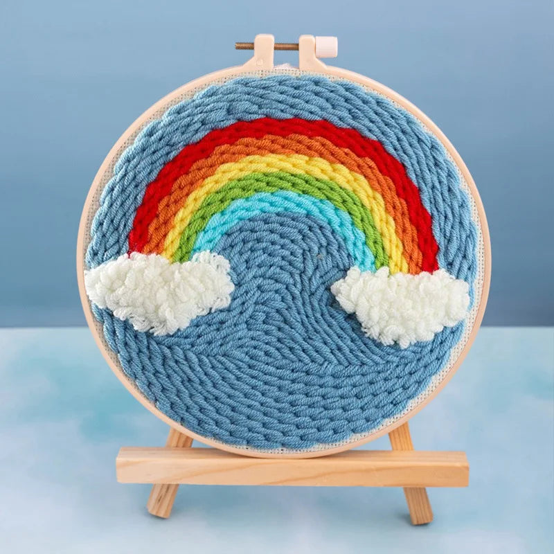 Kit de bordado con aguja mágica con diseño de arcoíris colorido sobre fondo azul, montado en soporte de madera.