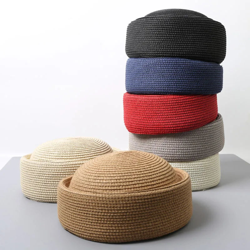 A stack of four straw pillbox sun hats in shades of black, blue, red, and beige.