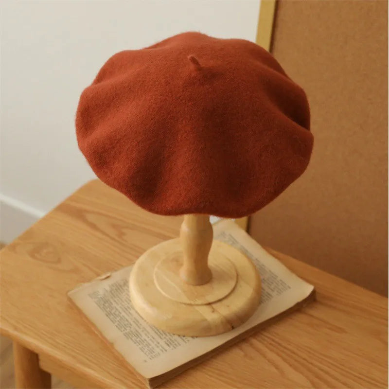 A terracotta orange wool beret hat displayed on a wooden stand.
