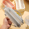 A hand holds a clear and gray 2-in-1 portable ice cube tray with a water bottle mold, next to pink and white silicone molds.