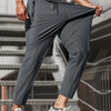 A muscular man wearing gray high-stretch joggers with black laces and white athletic shoes.