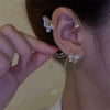 A close-up of a woman's ear showing a butterfly zircon ear cuff with a gold tassel earring.