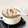 A white ceramic pot filled with light-colored dumplings served on a white spoon.