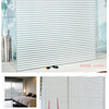 Primer plano de una película adhesiva blanca esmerilada para ventanas con patrón de rayas verticales instalada.