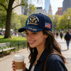 A smiling woman wearing a dark blue baseball cap embroidered with an eagle and text for the United States of America 250th An