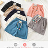 A collection of pastel and dark colored kids beach shorts laid out on a white surface.