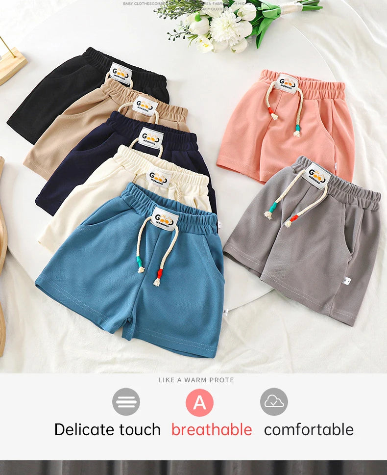 A collection of pastel and dark colored kids beach shorts laid out on a white surface.
