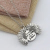Silver locket necklace featuring a detailed sunflower charm resting on a beige linen fabric.