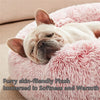 A white cat is sleeping on a pink fluffy plush pet bed.