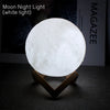 A white light moon night lamp shaped like a sphere resting on a wooden stand.