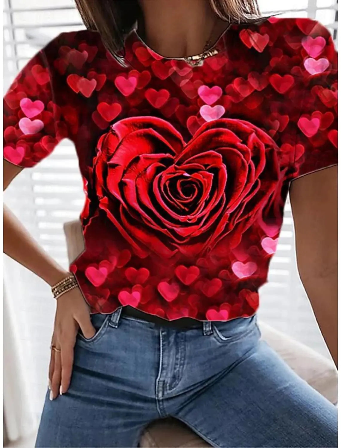 A woman models a red floral print t-shirt featuring a large rose design and small pink hearts, paired with blue jeans.