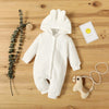 A white knitted hooded baby romper lying on a wooden surface with a small yellow smiley face card and a wooden toy.