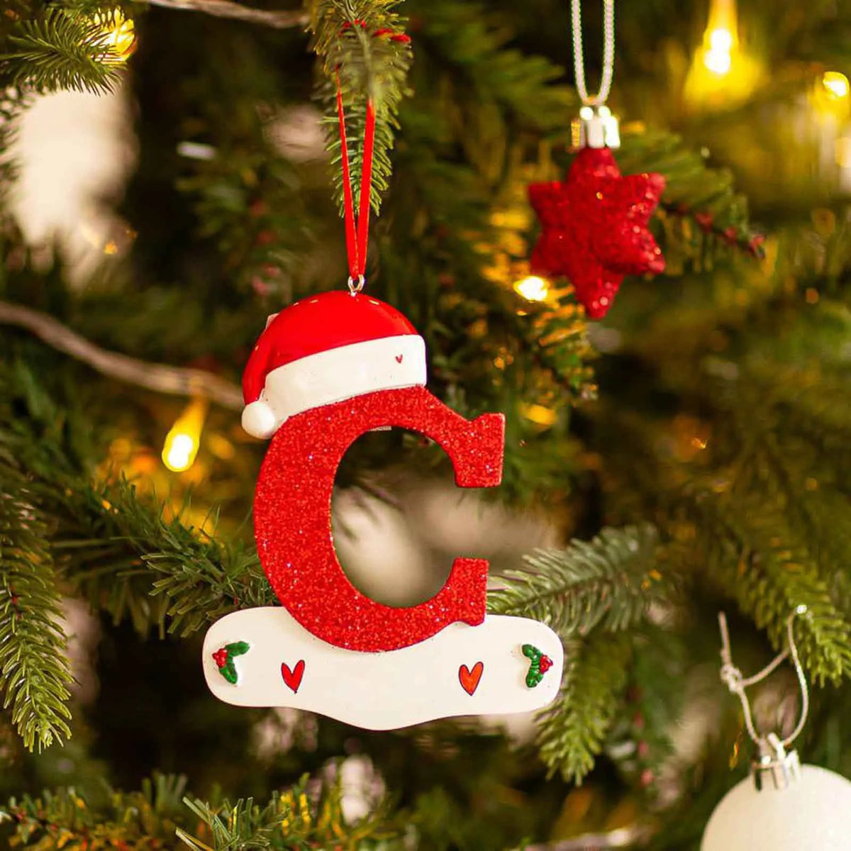 Rød akrylbokstav C som Santa-pynt henger på et grønt juletre.