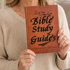 Une personne tient un guide d'étude biblique brun avec des lettres dorées sur un pull beige clair.