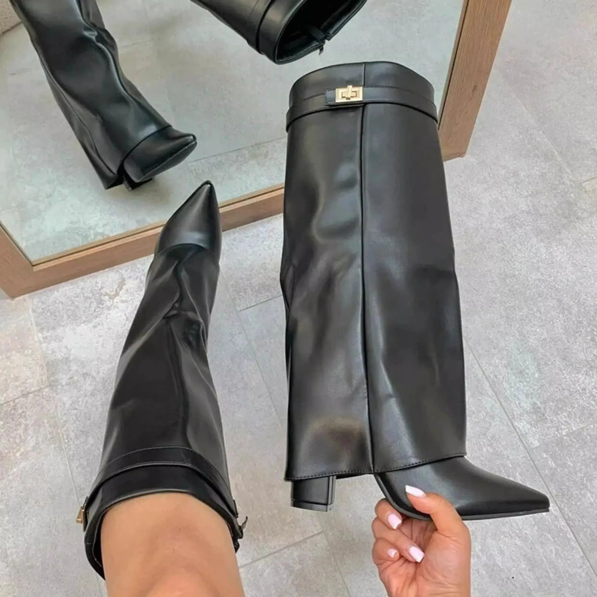 A pair of black knee-high chunky heel boots with a metal buckle displayed on a person's foot.