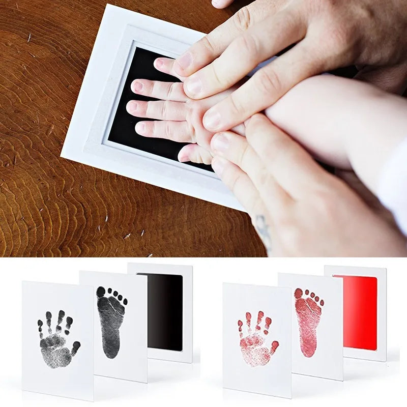 Hands pressing a white frame onto wood, showing an inkless baby handprint and footprint keepsake kit.