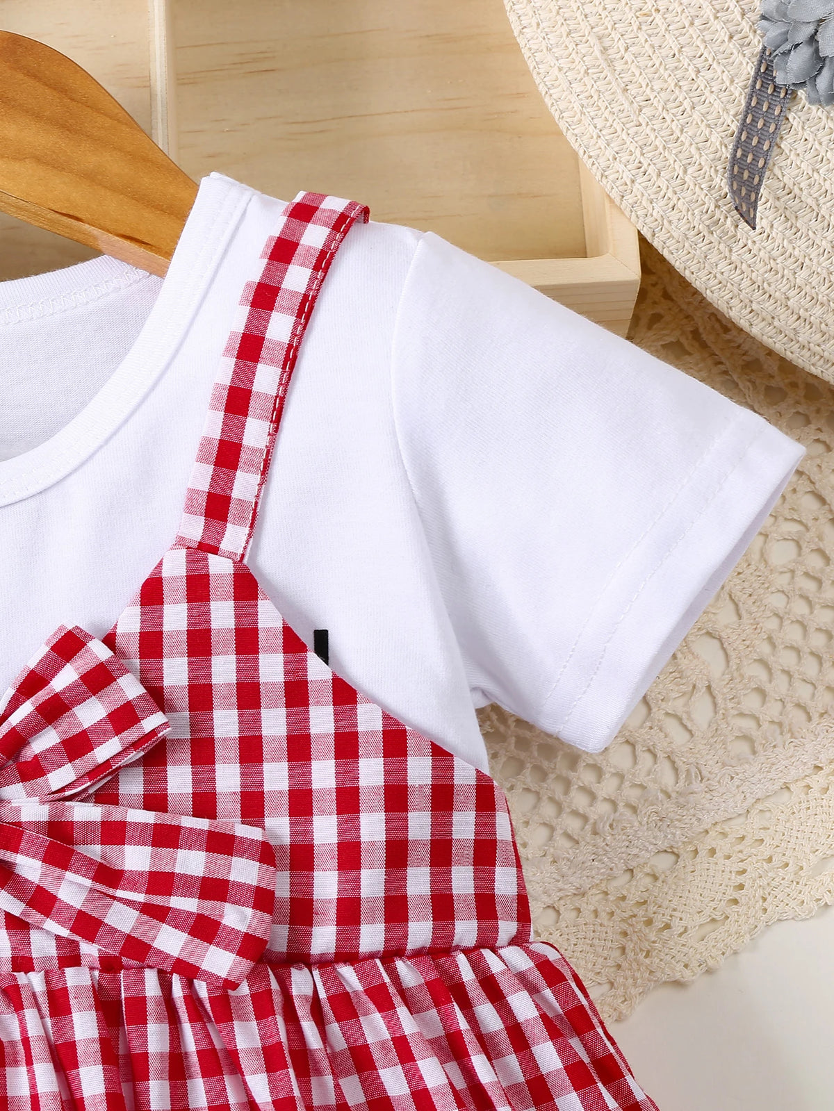 A white t-shirt with a red plaid apron worn by a child, resting on a beige knitted surface.