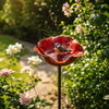 A handcrafted metal bird bath shaped like a flower, featuring a small bird perched on it in a garden setting.