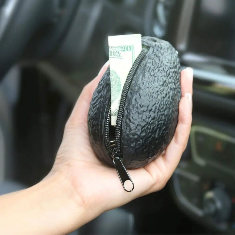 يد تمسك محفظة عملات أفوكادو سوداء بسحاب وداخلها ورقة نقدية من فئة عشرين دولارًا أمريكيًا.