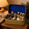 A classic nativity scene featuring figures of Mary Joseph and baby Jesus displayed inside a gold-colored metal tin box with a