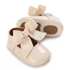 A pair of beige soft non-slip baby first walker shoes with satin bows.