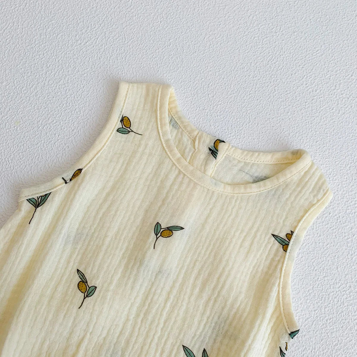 A cream-colored baby cotton sleeveless jumpsuit bodysuit set with small olive leaf embroidery.
