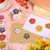 A collection of glitter flower round stickers in purple and orange are displayed on a white grid with craft supplies.