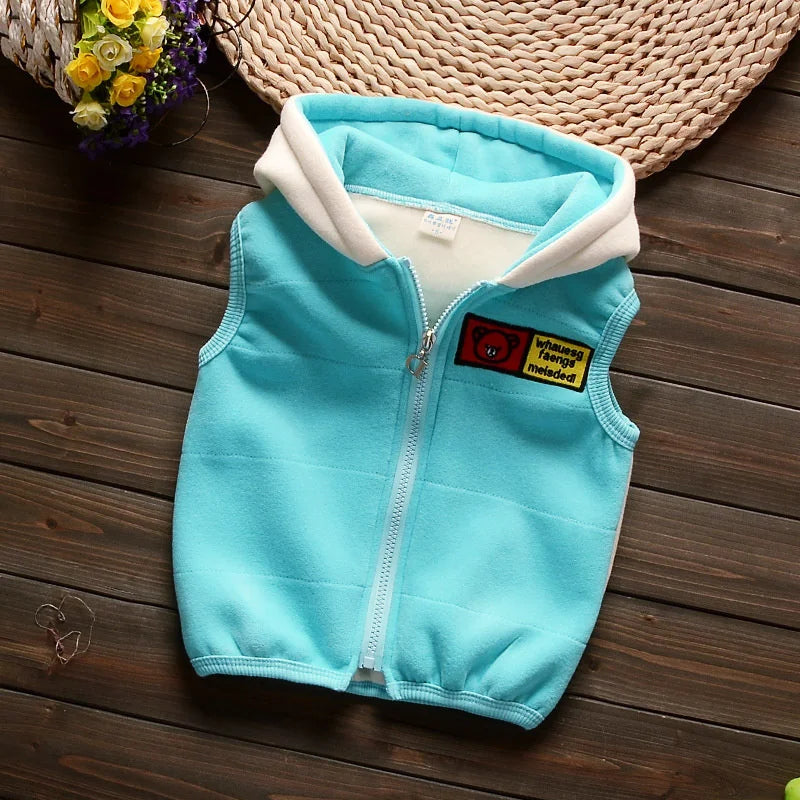 A light blue fleece zip-up vest with a cream lining and a yellow cartoon patch on a wooden surface.