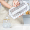 A hand is pouring ice cubes from a white mold into a glass of water, demonstrating the fun ice making product.