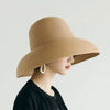 A woman wearing an elegant wide brim straw sun hat in beige against a light background.