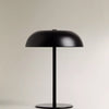 A black portable touch table lamp with a dome shade and a slender stand on a light background.