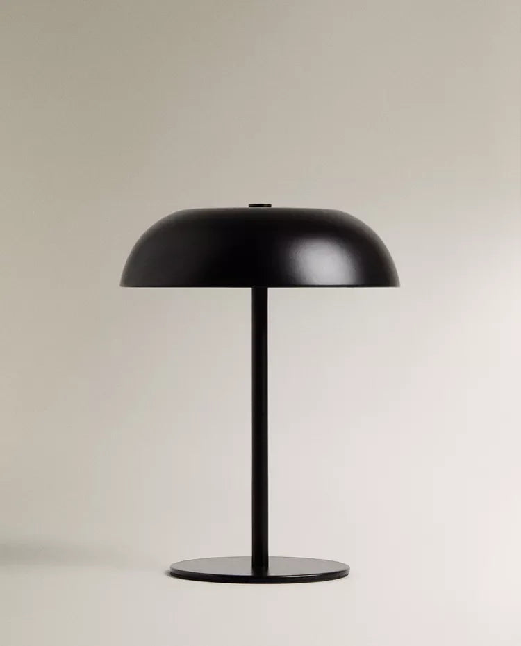 A black portable touch table lamp with a dome shade and a slender stand on a light background.