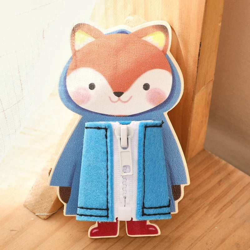 A felted fox character wearing a blue coat and red boots, used as a Montessori wooden busy board for children's practice.