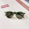 A pair of olive green sunglasses resting on a white surface with a handwritten note nearby.