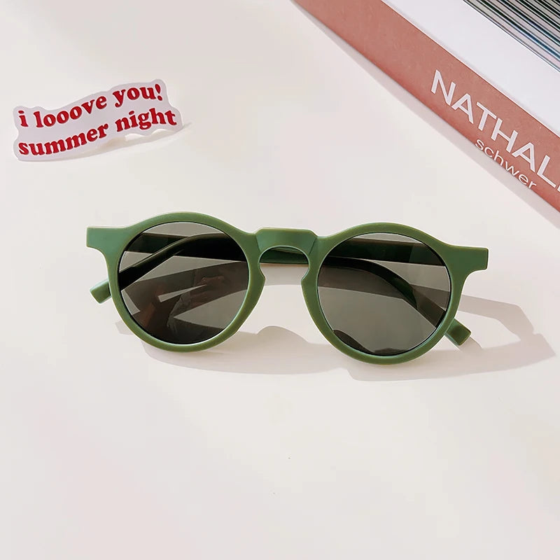 A pair of olive green sunglasses resting on a white surface with a handwritten note nearby.