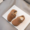 A pair of brown retro non-slip kids' moccasin shoes with a brass hook-and-loop closure displayed on a white card.