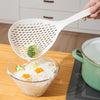 A hand is holding a white long-handled kitchen strainer spoon over a glass bowl filled with clear noodles.