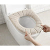 A hand is placing a beige, textured acrylic toilet seat cover onto a white toilet bowl.