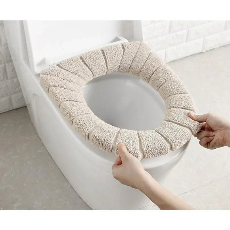 A hand is placing a beige, textured acrylic toilet seat cover onto a white toilet bowl.