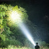A strong light beam shoots far away from a person in a grassy outdoor setting at night.